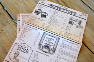 Un menu au design inspiré des journaux du début du XXe siècle, avec illustrations gravées et typographie rétro.
